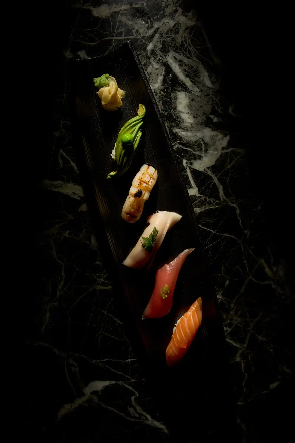 Nigiri-Sushi Variation mit Edelfisch und Avocado auf schwarzem Teller